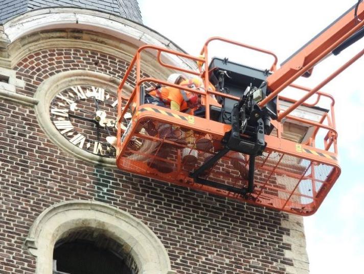 Image of an orange crane with a worker on it doing maintenance work on a building with bricks.