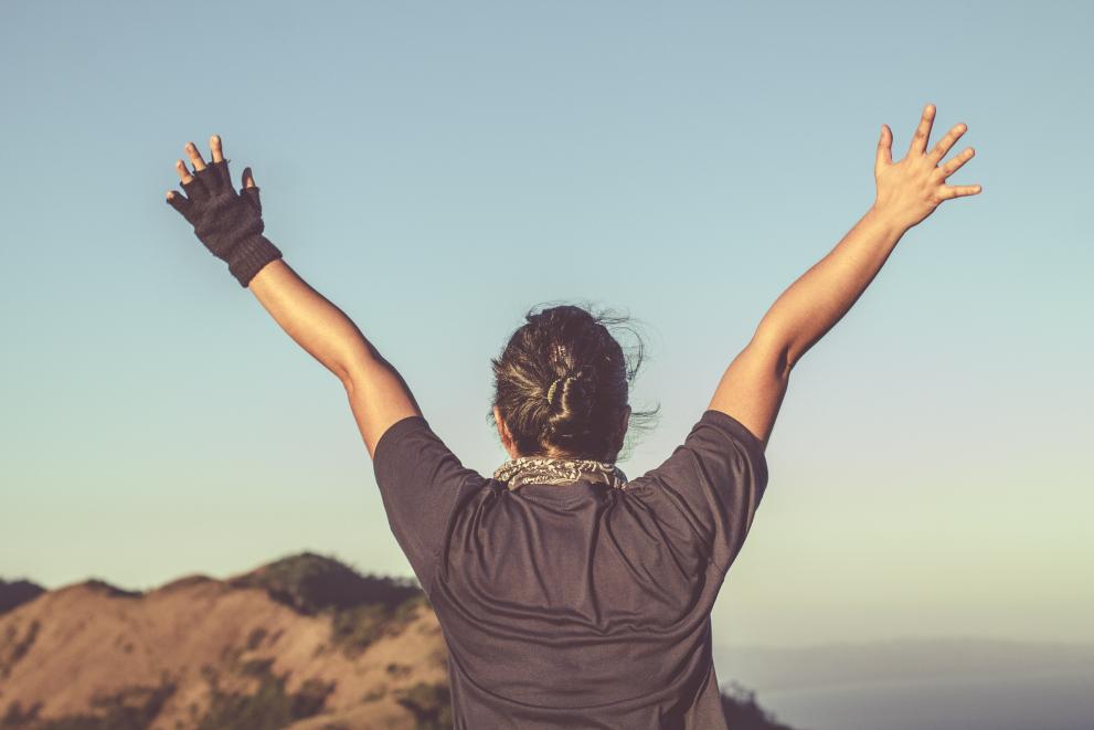 Person with open arms up towards the sky in front of a landscape