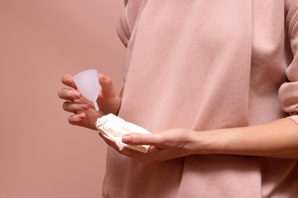 Pink background image with a person holding a light-coloured cloth bag and a menstrual cup.